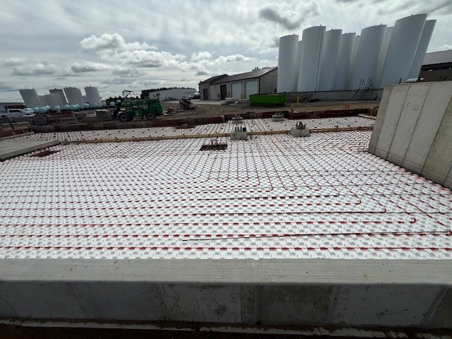 heated floors being installed on a new dry fertilizer storage and blending building with fertilizer tanks in the background